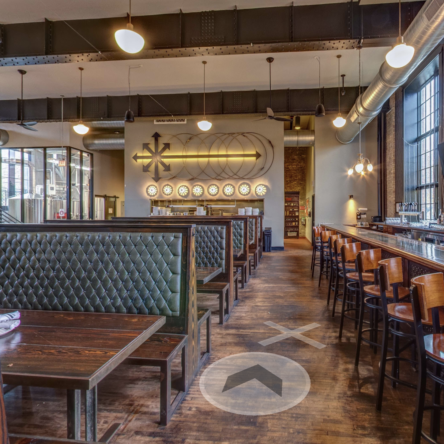 wide shot of main dining room of Eris Brewery & Ciderhouse, the kitchen window is on the far side of the room, to the right is the main bar, and to the left of it is the brew room, encased in large windows.