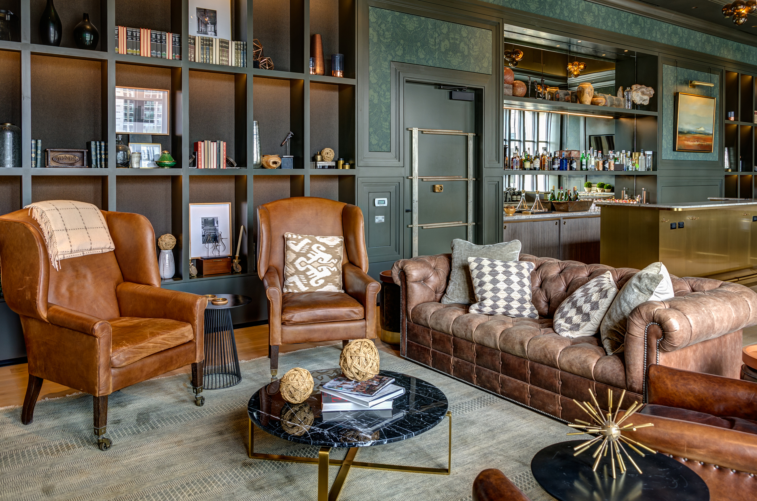 Lounge area with leather sofa, leather chairs, book case on the wall and a door that resembles a vault door
